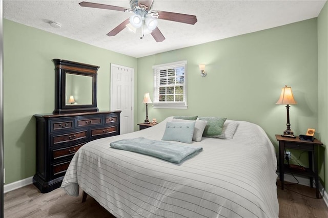 bedroom with baseboards, wood finished floors, a closet, a textured ceiling, and a ceiling fan