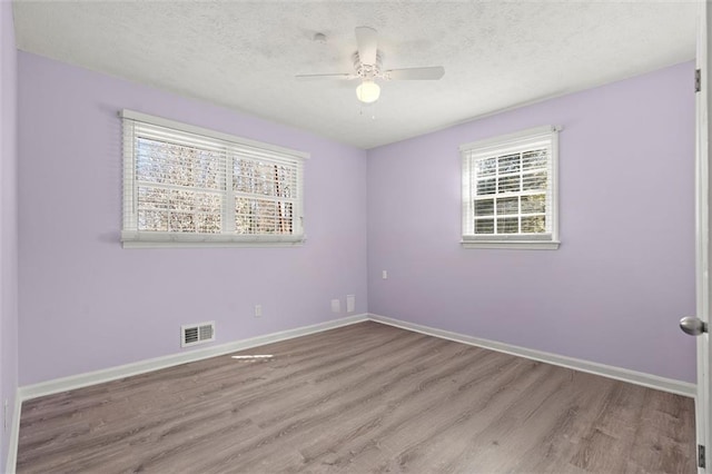 unfurnished room featuring a textured ceiling, wood finished floors, visible vents, and baseboards