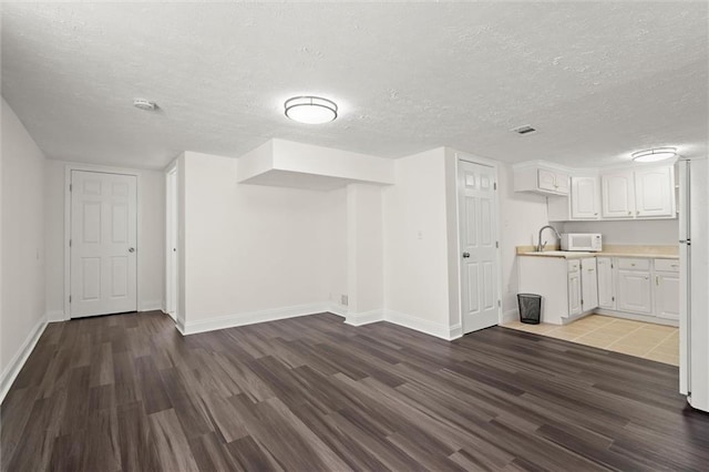 unfurnished living room featuring baseboards, dark wood-style flooring, and a textured ceiling