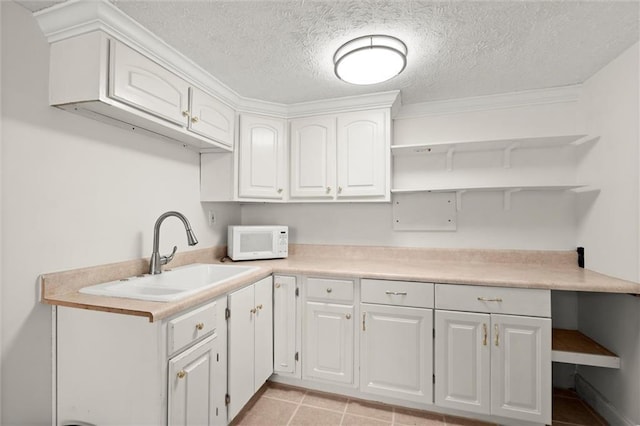 kitchen featuring white microwave, open shelves, light countertops, white cabinets, and a sink