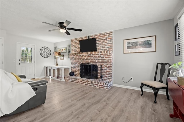 living room featuring a fireplace, a textured ceiling, baseboards, and wood finished floors