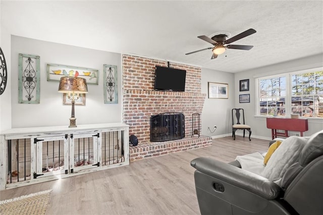 living room with ceiling fan, baseboards, a fireplace, wood finished floors, and a textured ceiling