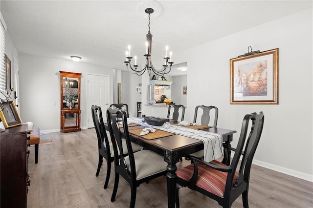 dining area with baseboards, an inviting chandelier, and light wood finished floors