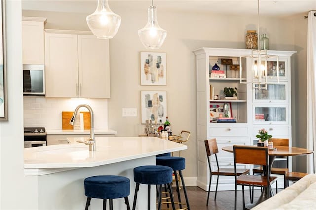 kitchen with decorative backsplash, hanging light fixtures, stainless steel appliances, light countertops, and white cabinetry