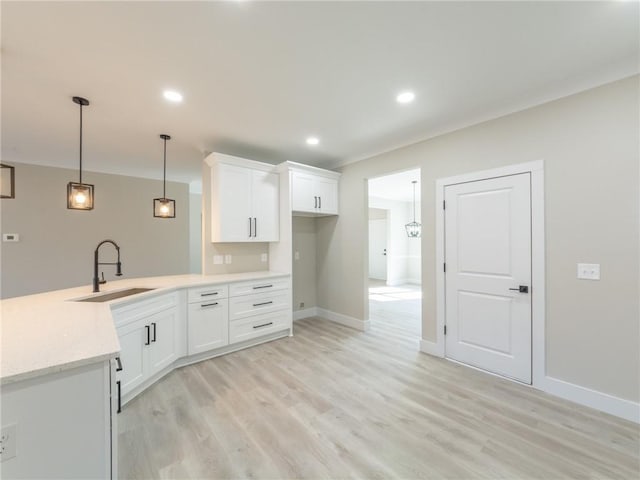 kitchen with hanging light fixtures, white cabinets, sink, and light hardwood / wood-style flooring