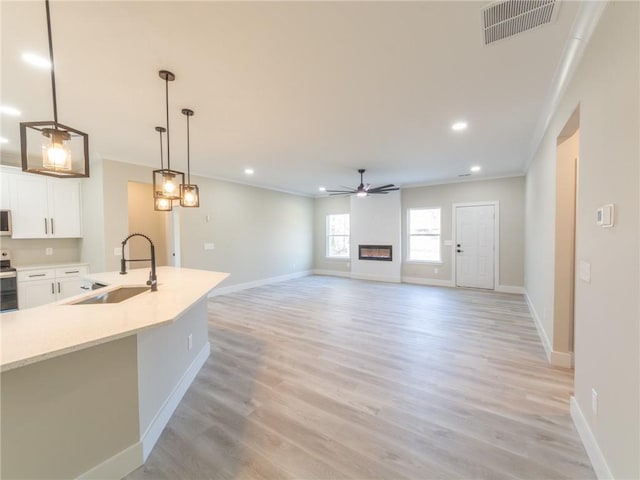 kitchen featuring stainless steel range with electric stovetop, hanging light fixtures, crown molding, white cabinets, and sink