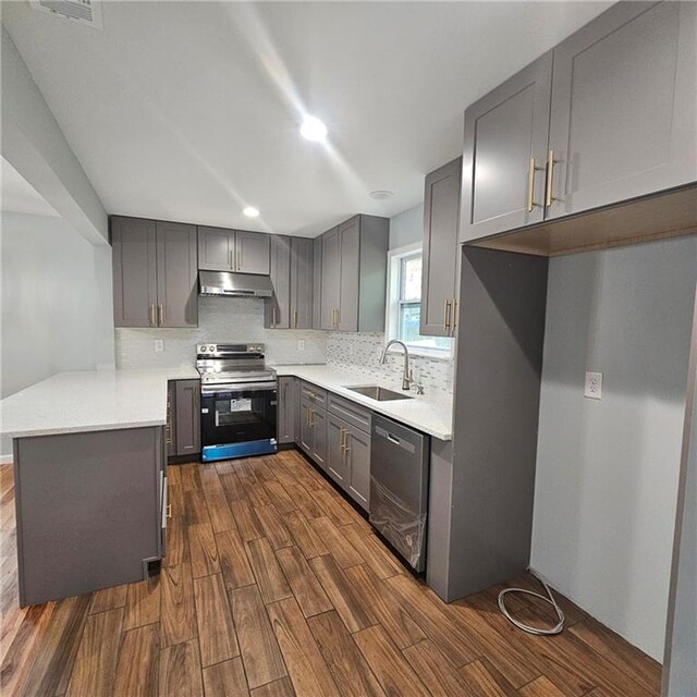 487 Eastside Dr, Dacula, GA 30019 - kitchen with appliances with stainless steel finishes, gray cabinetry, a sink, under cabinet range hood, and dark wood-style floors