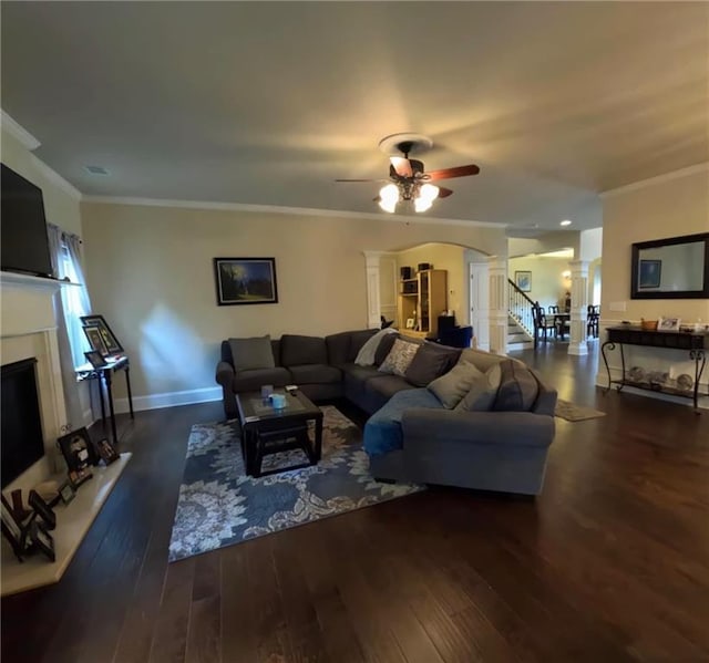 living area featuring ceiling fan, a fireplace with raised hearth, ornamental molding, ornate columns, and hardwood / wood-style floors