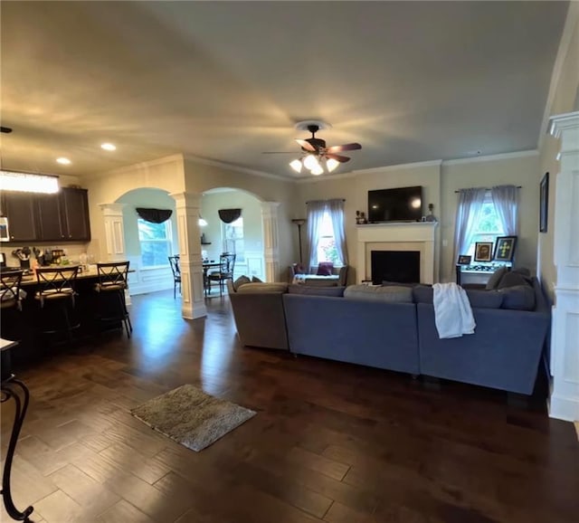 living area with ornate columns, arched walkways, a ceiling fan, and plenty of natural light