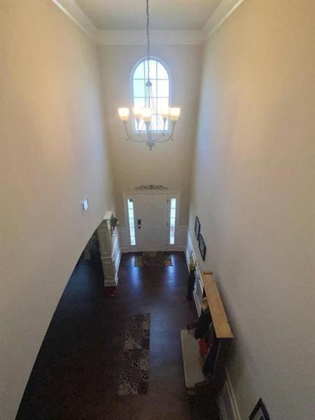 entryway with ornamental molding, wood finished floors, a towering ceiling, and an inviting chandelier