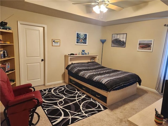 carpeted bedroom with a tray ceiling, ceiling fan, and baseboards