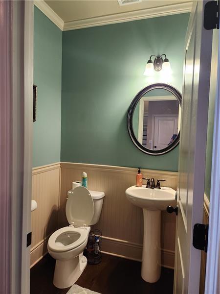 bathroom with wainscoting, wood finished floors, toilet, and crown molding