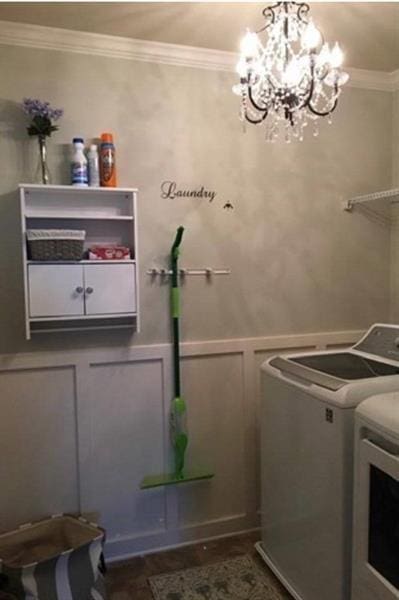 clothes washing area featuring washer and dryer, laundry area, a decorative wall, a chandelier, and ornamental molding