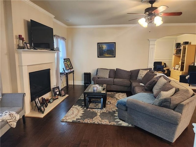 living room with ceiling fan, crown molding, arched walkways, wood-type flooring, and a fireplace with raised hearth