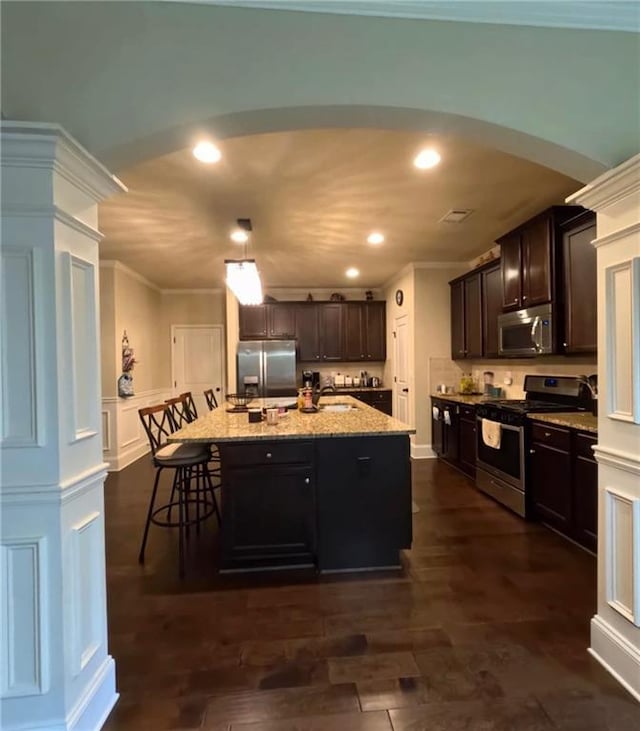 kitchen with recessed lighting, arched walkways, appliances with stainless steel finishes, and light stone counters