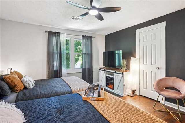 877 Lee Andrews Ave SE, Atlanta, GA 30315 - bedroom featuring a textured ceiling, a glass covered fireplace, visible vents, a ceiling fan, and wood finished floors