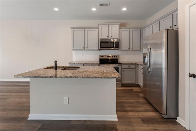 kitchen with appliances with stainless steel finishes, light stone countertops, dark wood-type flooring, and an island with sink