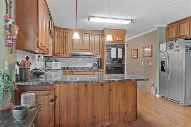 kitchen featuring dobule oven black, white microwave, a peninsula, under cabinet range hood, and stainless steel refrigerator with ice dispenser