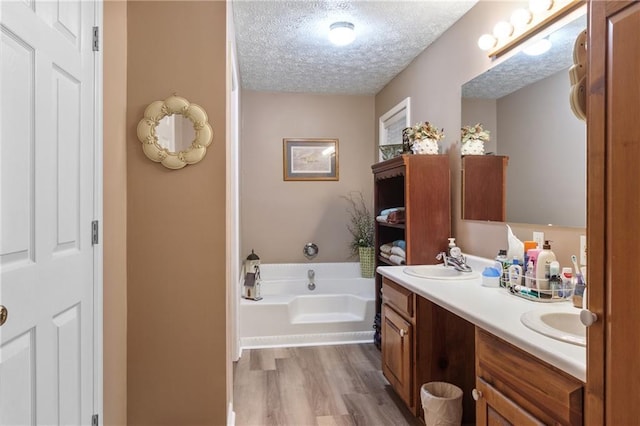 full bathroom with double vanity, wood finished floors, a garden tub, a textured ceiling, and a sink