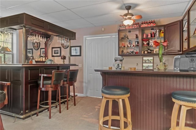 bar featuring a paneled ceiling, a ceiling fan, indoor wet bar, and light colored carpet