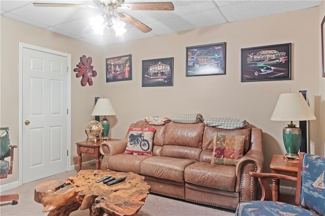 living room with ceiling fan, baseboards, a drop ceiling, and carpet flooring