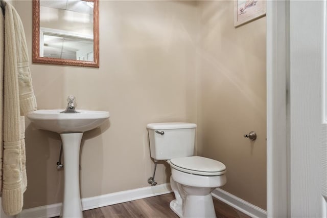 half bath with baseboards, toilet, and wood finished floors