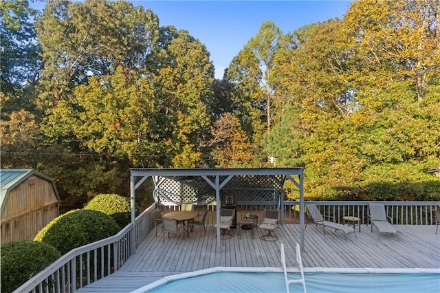 view of pool featuring outdoor dining area, an outdoor structure, a wooden deck, and a storage shed