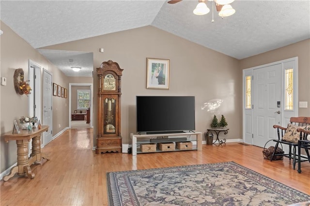 living area with vaulted ceiling, a textured ceiling, wood finished floors, and baseboards