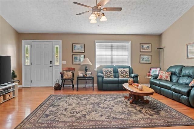 living area with baseboards, a textured ceiling, a ceiling fan, and wood finished floors