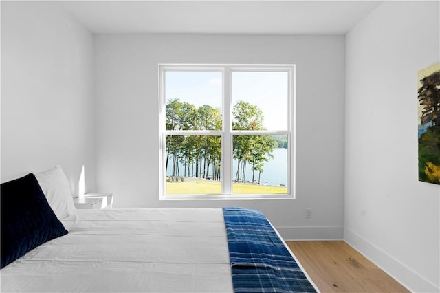 bedroom with multiple windows, hardwood / wood-style flooring, and a water view