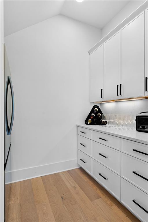 bar with light wood-type flooring, refrigerator, white cabinetry, and vaulted ceiling