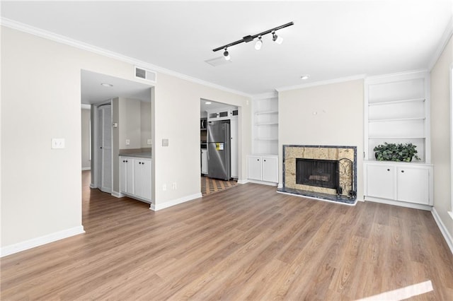 unfurnished living room with built in shelves, light hardwood / wood-style floors, ornamental molding, and track lighting