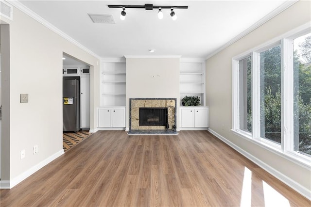 unfurnished living room featuring a stone fireplace, plenty of natural light, ornamental molding, and hardwood / wood-style flooring