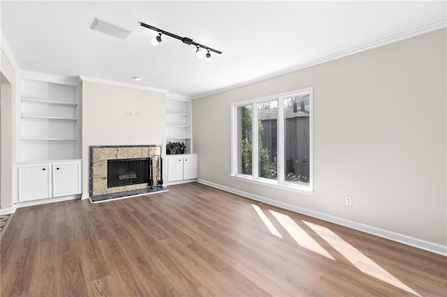 unfurnished living room with hardwood / wood-style floors, built in shelves, ornamental molding, and track lighting