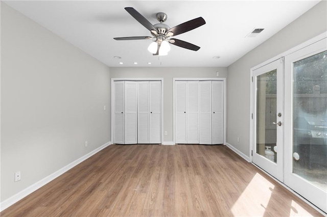 unfurnished bedroom featuring french doors, ceiling fan, access to exterior, light wood-type flooring, and multiple closets