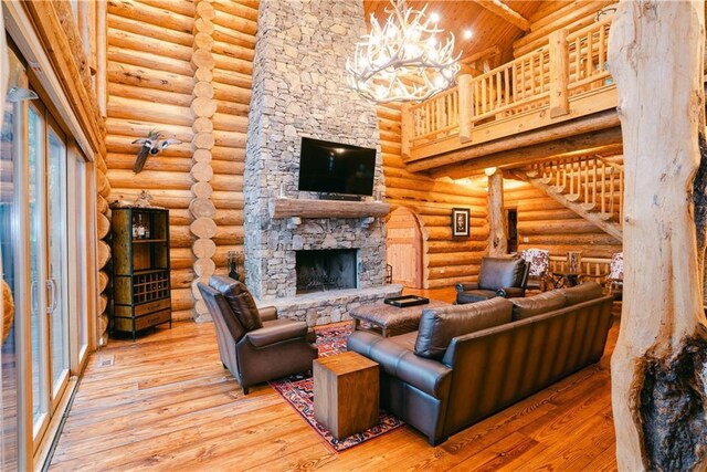 living room featuring light hardwood / wood-style floors, an inviting chandelier, a high ceiling, a stone fireplace, and rustic walls