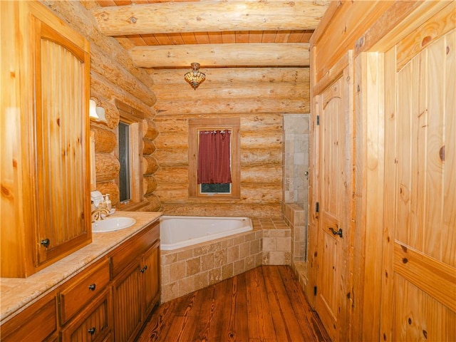 bathroom with beam ceiling, tiled bath, log walls, hardwood / wood-style flooring, and vanity