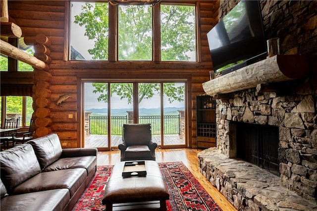 living room with a high ceiling, a stone fireplace, log walls, and wood-type flooring