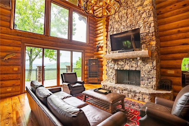 living room with an inviting chandelier, a towering ceiling, a fireplace, wood-type flooring, and rustic walls