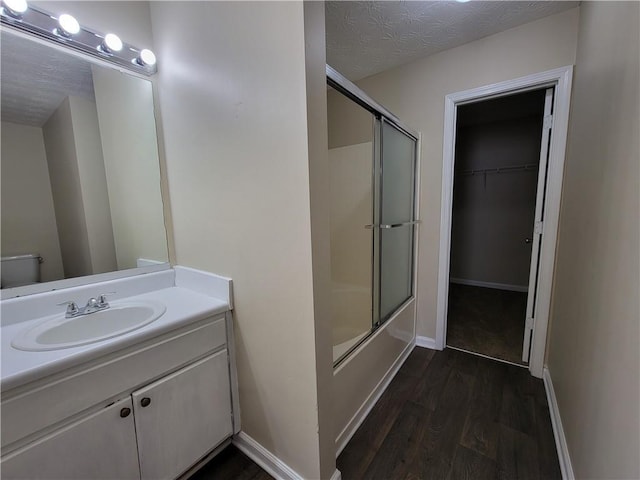 full bathroom featuring baseboards, wood finished floors, combined bath / shower with glass door, a textured ceiling, and vanity