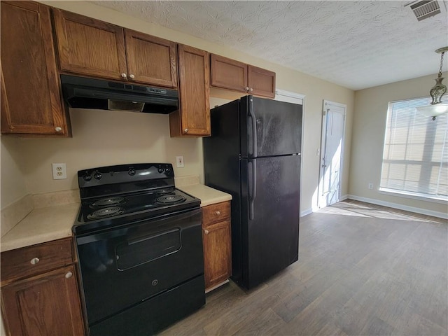 kitchen with light countertops, under cabinet range hood, black appliances, and wood finished floors