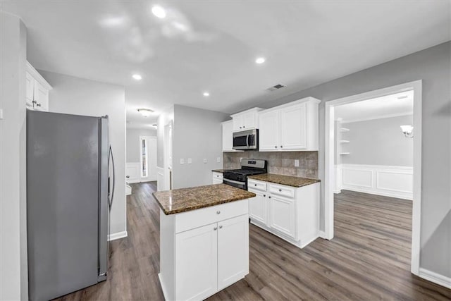 kitchen with white cabinets, appliances with stainless steel finishes, dark stone counters, and a center island