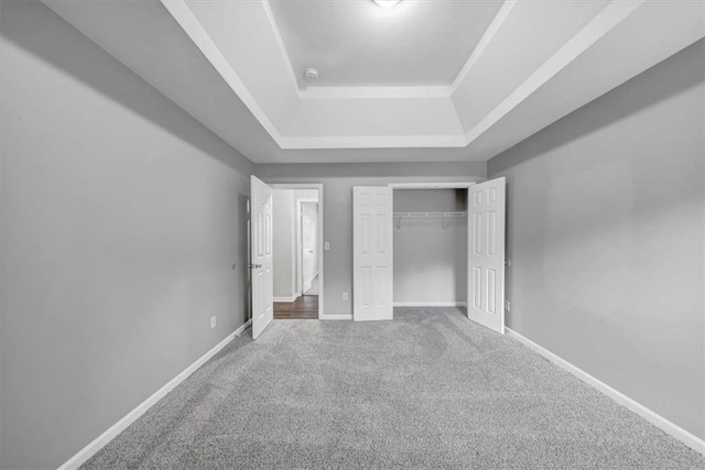 unfurnished bedroom with carpet, a tray ceiling, and a closet