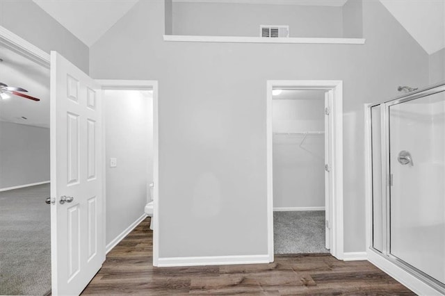 unfurnished bedroom featuring ceiling fan, a walk in closet, high vaulted ceiling, and dark hardwood / wood-style flooring