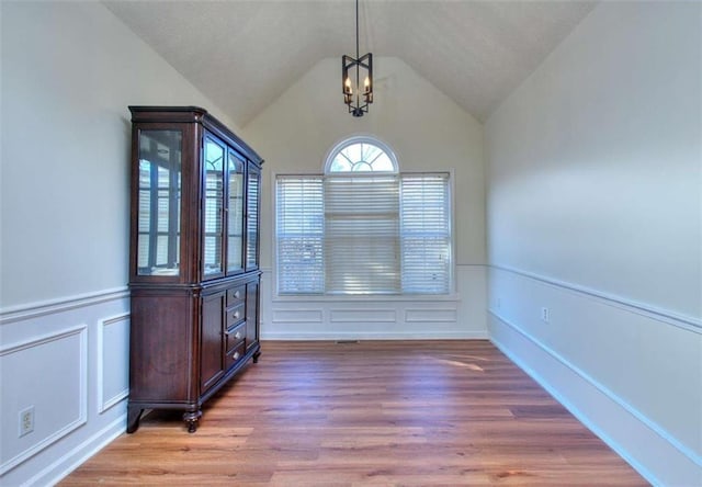 unfurnished dining area with hardwood / wood-style flooring, vaulted ceiling, and an inviting chandelier