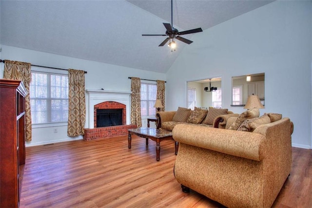 living room with hardwood / wood-style floors, ceiling fan with notable chandelier, a fireplace, and high vaulted ceiling