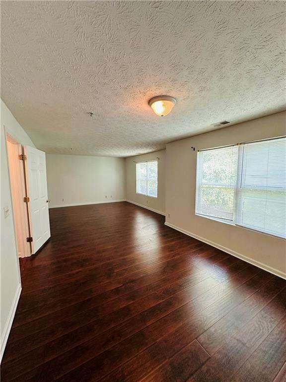 empty room with dark wood finished floors, visible vents, a textured ceiling, and baseboards