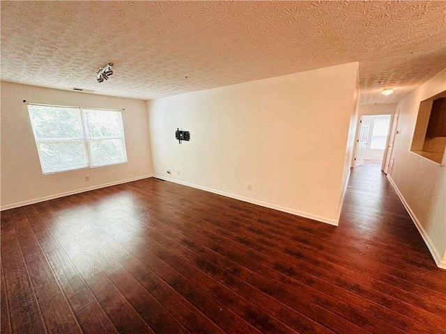 empty room featuring baseboards, a textured ceiling, and dark wood finished floors