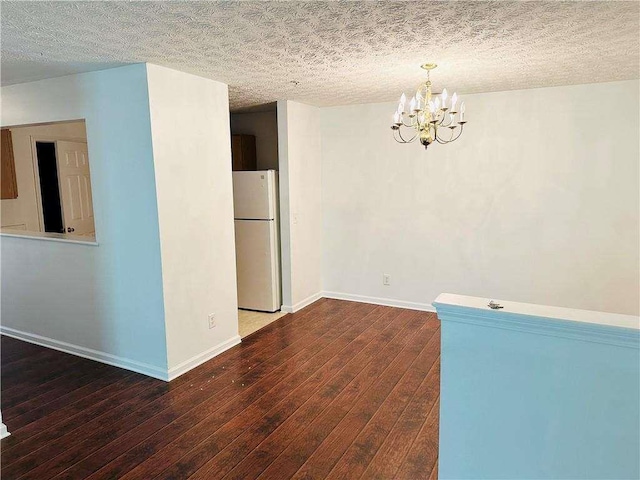 empty room featuring baseboards, a textured ceiling, an inviting chandelier, and hardwood / wood-style floors