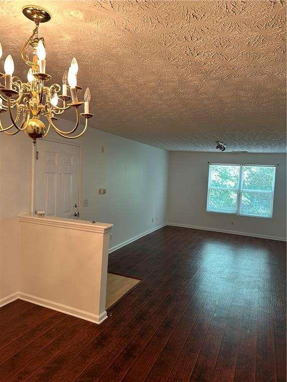 spare room featuring dark wood finished floors, a notable chandelier, a textured ceiling, and baseboards